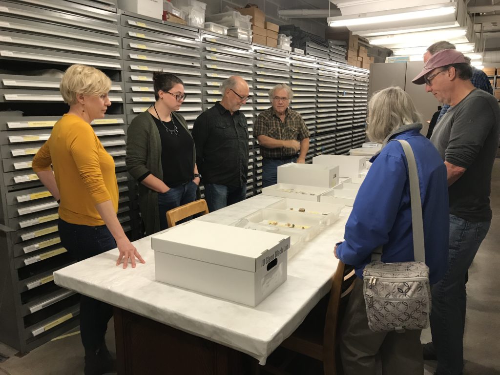 Group of people around artifacts on table in type collection room.